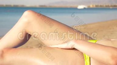 漂亮的腿的女孩在海洋背景上擦进皮肤防晒霜。 高清高清